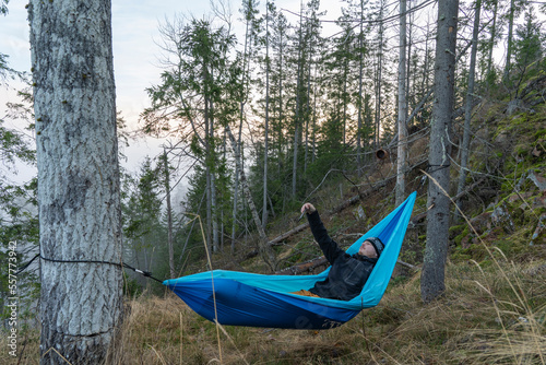 Man taking a selfie on a smartphone while lying in a hammock in the woods.