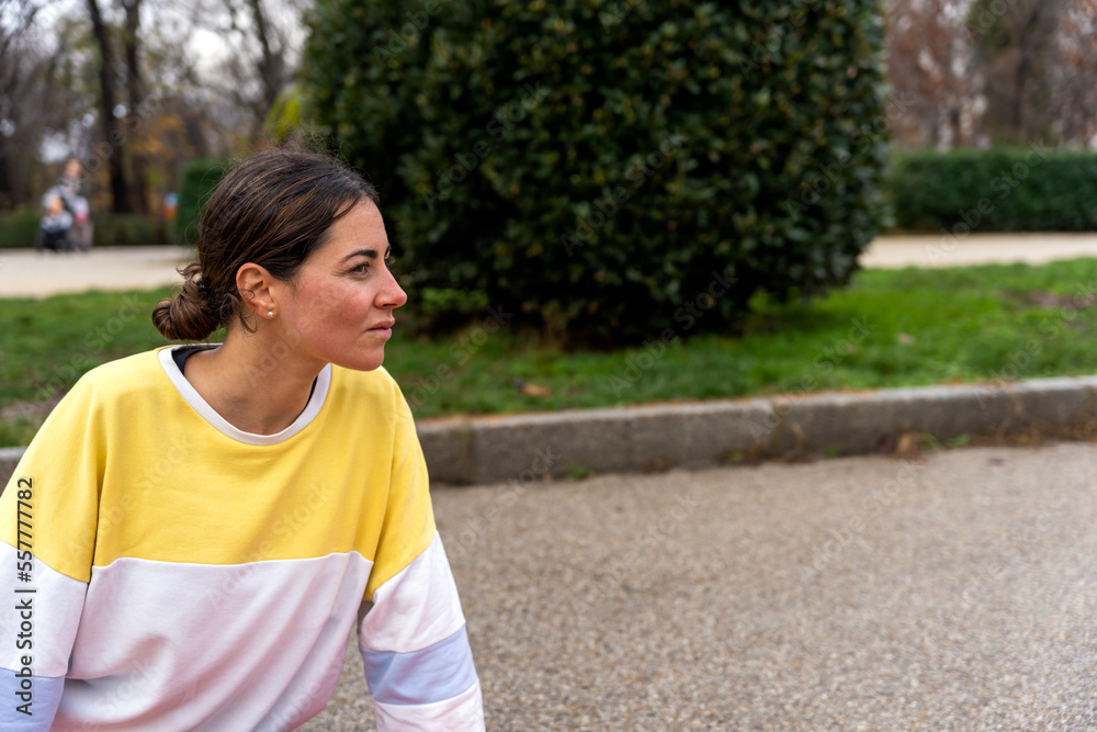 Young female in sweatshirt looking away attentively while sitting against blurred background of green park in summertime Young female in sweatshirt looking away attentively while sitting against blurred background of green park in summertime