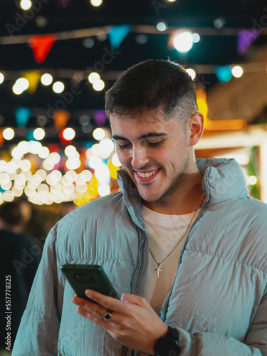 Hombre joven feliz mirando su teléfono móvil en una calle llena de luces