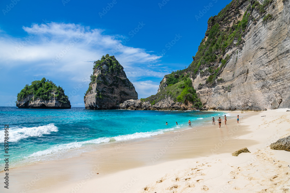 BALI / INDONESIA - NOVEMBER 8, 2022: People swimming at the beautiful sandy beach (Diamond beach) with rocky mountains and clear water in Nusa Penida.