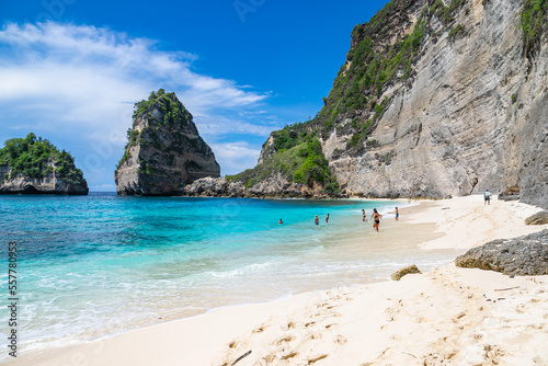 BALI / INDONESIA - NOVEMBER 8, 2022: People swimming at the beautiful sandy beach (Diamond beach) with rocky mountains and clear water in Nusa Penida.