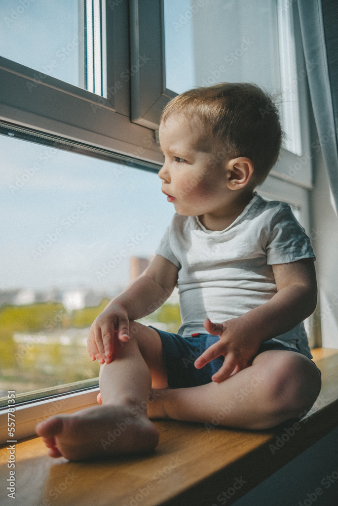 Little cute attractive boy sitting on windowsill and look at window