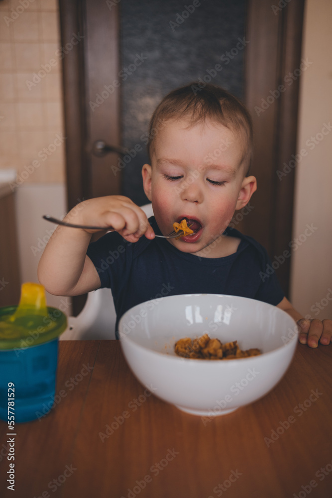 a child eats pasta from a white cup at the kitchen table a child eats pasta from a white cup at the kitchen table