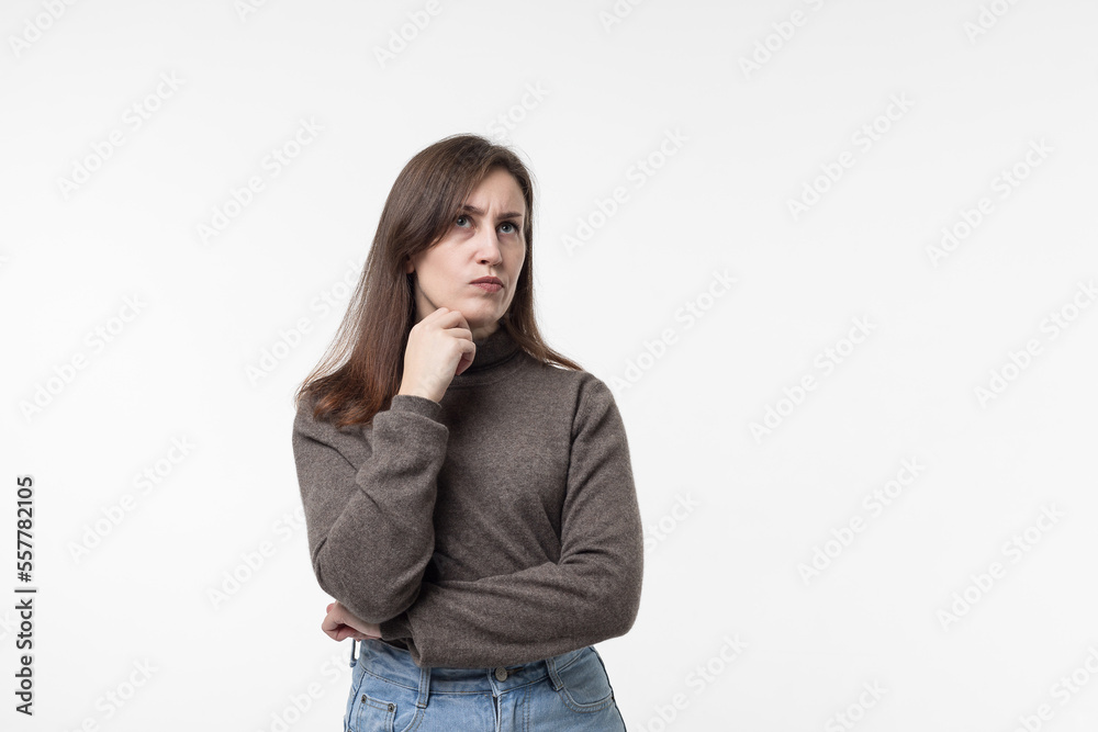 portrait of pretty confident thoughtful girl,holding hand near the face, looking seriously up,standing over white background.young woman thinking worried about a question,concerned and nervous. portrait of pretty confident thoughtful girl,holding hand near the face, looking seriously up,standing over white background.young woman thinking worried about a question,concerned and nervous.
