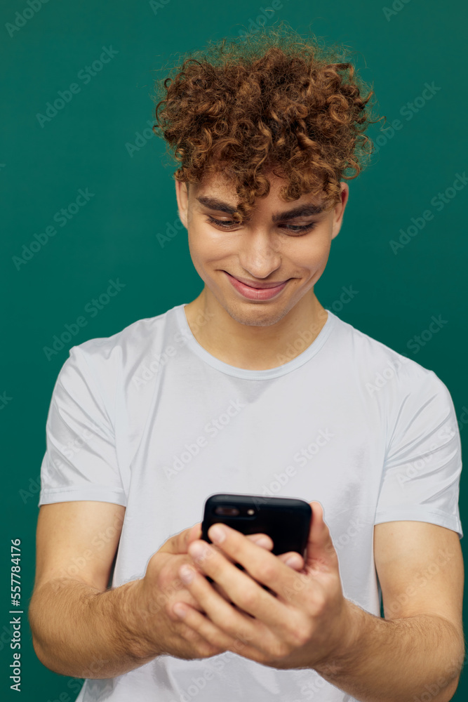a funny, joyful man with curly hair stands against a green background and holds his smartphone with both hands, carefully looking into it. vertical photography in the studio a funny, joyful man with curly hair stands against a green background and holds his smartphone with both hands, carefully looking into it. vertical photography in the studio