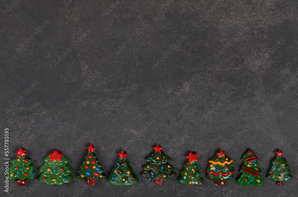 Holiday sweets. Cute Candies in the shape of various Christmas trees, covered with colored icing sugar. Dark gray background. Top view. Copy space