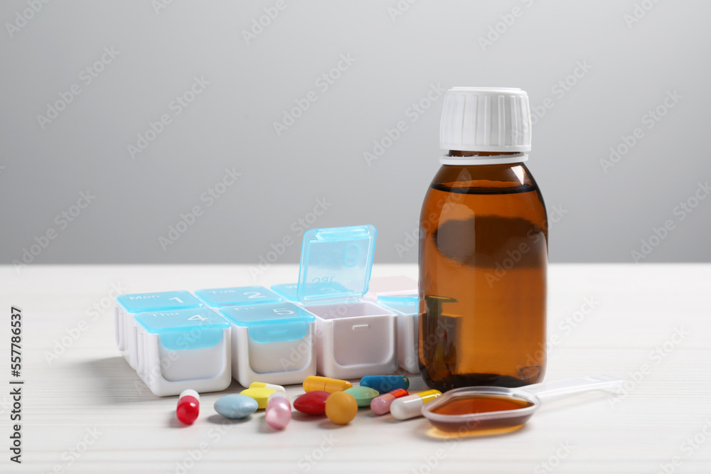 Bottle of syrup, dosing spoon and pills on white table against light grey background. Cold medicine Bottle of syrup, dosing spoon and pills on white table against light grey background. Cold medicine