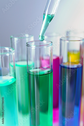 Dripping liquid from pipette into test tube on grey background, closeup
