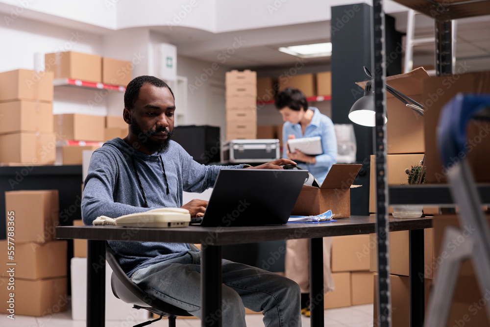 African american employee sitting at desk in warehouse delivery ...