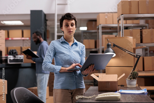 Warehouse supervisor holding laptop checking shipping detalies while working at customers orders, putting packages in carton box preparing for delivery. Distribution center fulfillment company photo