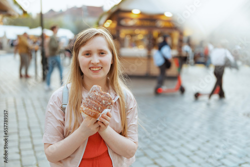 Photography smiling girl in jacket at fair in city eating trdelnik