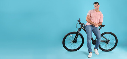 Handsome young man with bicycle on light blue background, space for text. Banner design
