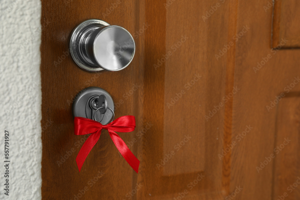 Fototapeta premium House key with red bow in door lock, closeup. Housewarming party