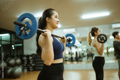 young asian woman lifting barbell in front of chest during exercise in fitness room © Odua Images