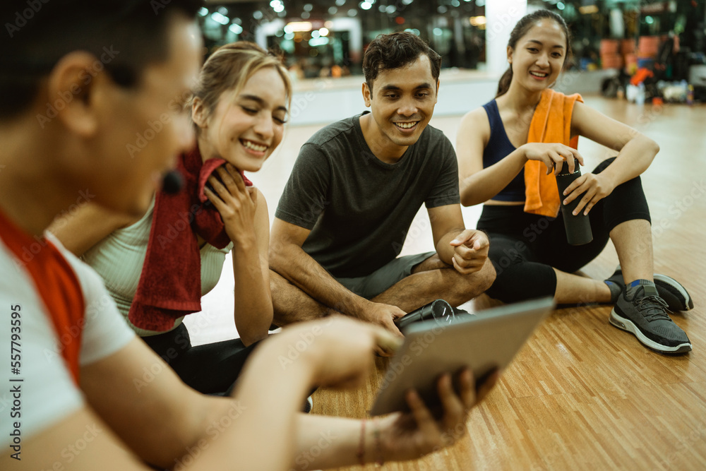 male instructor showing his pad screen to athletic young people while sitting on the floor after practice male instructor showing his pad screen to athletic young people while sitting on the floor after practice