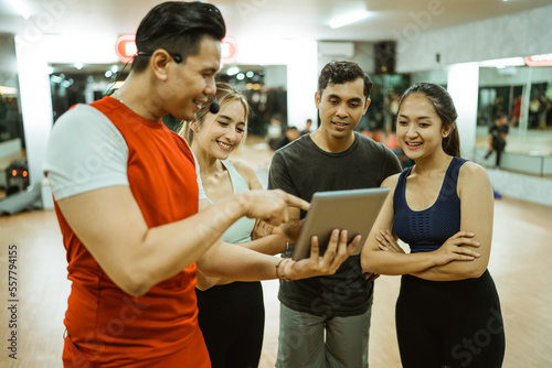 male instructor showing tablet to young sporty people during exercise break in gym