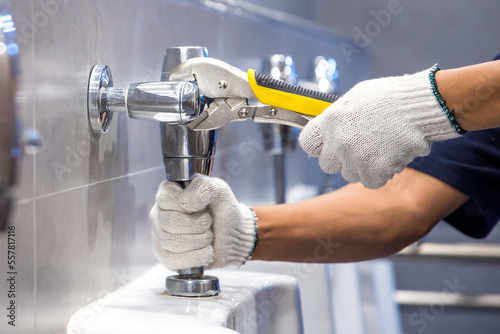 Hand of handyman or plumber is using a wrench to fix or repair leaking water pipes, faucets or valves in toilet bowls and sinks in restroom or bathroom