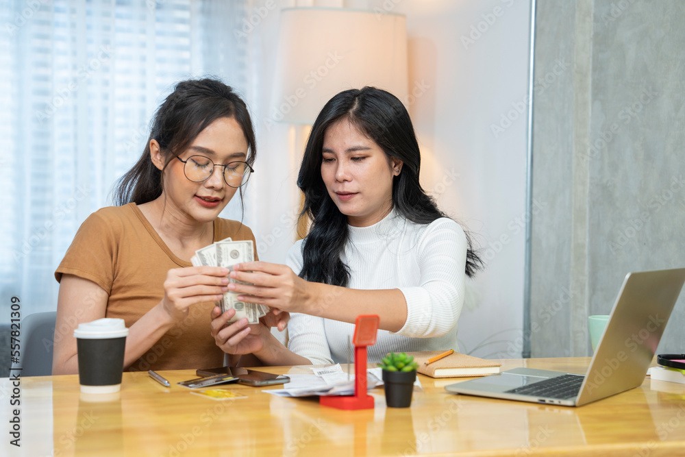 Asian sisters counting money for financial management in paying house expenses, apartment rent, water bill, electricity bill, credit card bills due, paying through banking application and laptop. Asian sisters counting money for financial management in paying house expenses, apartment rent, water bill, electricity bill, credit card bills due, paying through banking application and laptop.