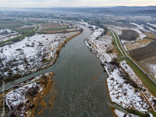 Obraz na płótnie Aerial view. Flowing river seen from above. A view of the mountains on the horizon. Snow, sun, landscape, nature, park. w salonie
