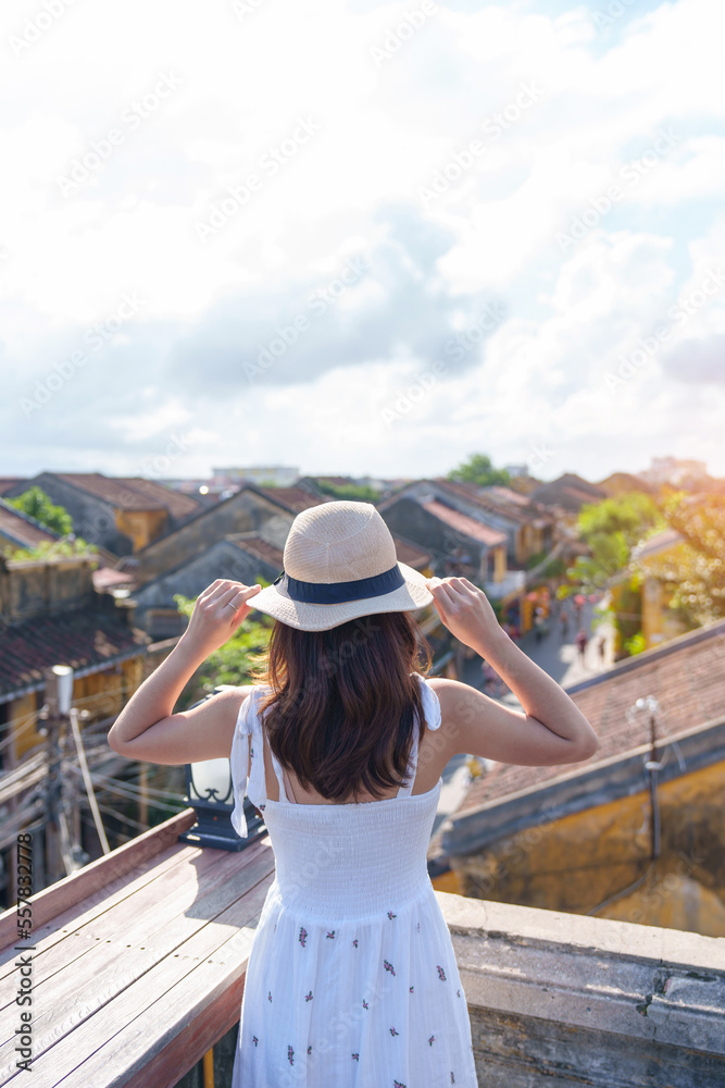 happy traveler traveling at Hoi An ancient town in Vietnam, woman with dress and hat sightseeing view at rooftop.landmark and popular for tourist attractions. Vietnam and Southeast Asia travel concept