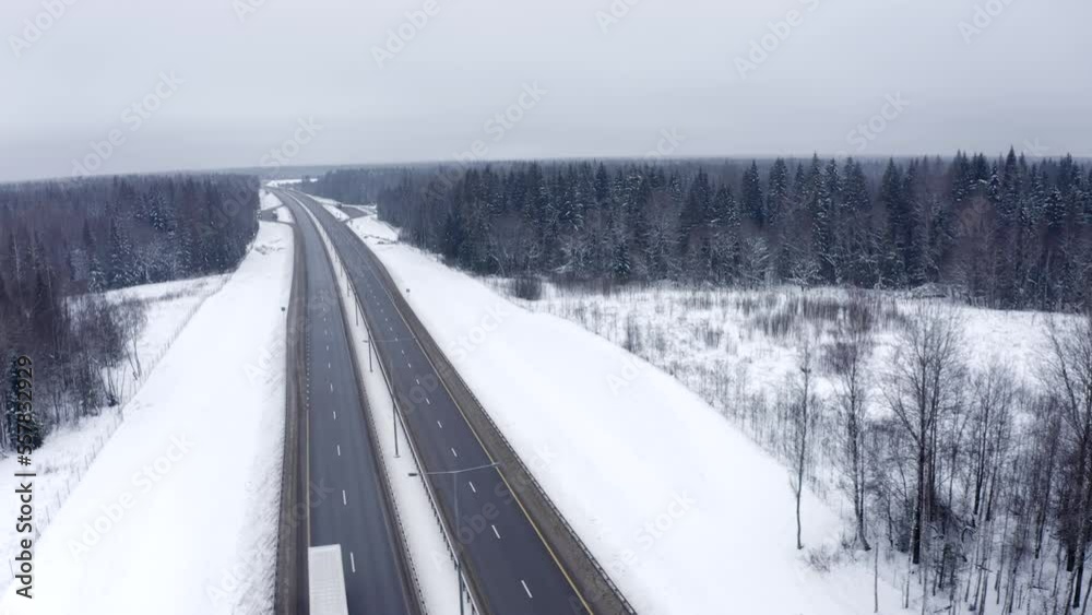 Flying the drone sideways to the left over a highway with two trucks passing through snow-covered trees in winter. Two trucks drive along the road in winter in the forest aerial view. Flying the drone sideways to the left over a highway with two trucks passing through snow-covered trees in winter. Two trucks drive along the road in winter in the forest aerial view.