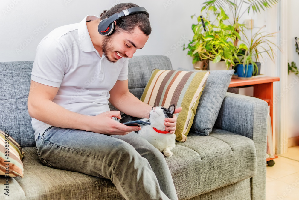Positive man listening music with headphones, seat on sofa.