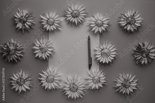 Blank sheet of paper with copy space for text, pen and dimensional paper flowers close-up top view DIY grey background. Place for congratulations or wishes. Christmas decor. Blurred background.