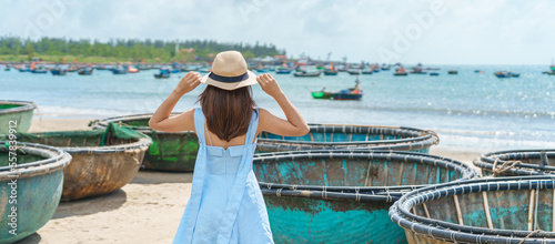 Woman traveler visiting at My Khe beach and sightseeing basket finishing boats. Tourist with blue dress and hat traveling in Da Nang city. Vietnam and Southeast Asia travel concept