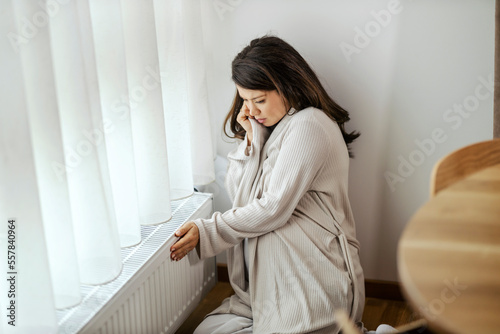 A pregnant woman is checking on radiator if it is warm.