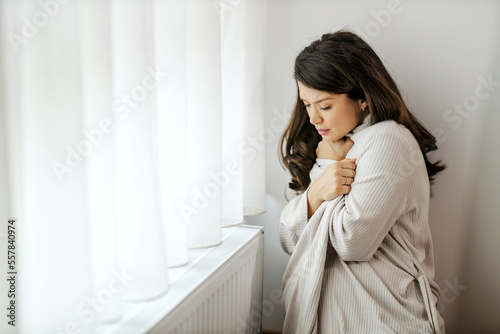 A pregnant woman is trying to warm herself up while sitting next to a cold radiator.