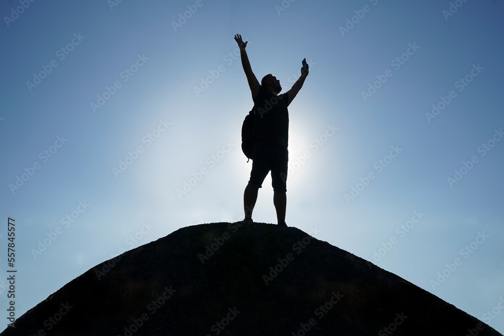 Silhouette man rising hands standing on the top view on the picturesque sunrise background. watching sunset. freedom concept ! mobile cell phone in male hand. Silhouette man rising hands standing on the top view on the picturesque sunrise background. watching sunset. freedom concept ! mobile cell phone in male hand.