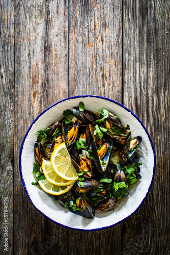 Cooked mussels with lemon and parsley on wooden table
