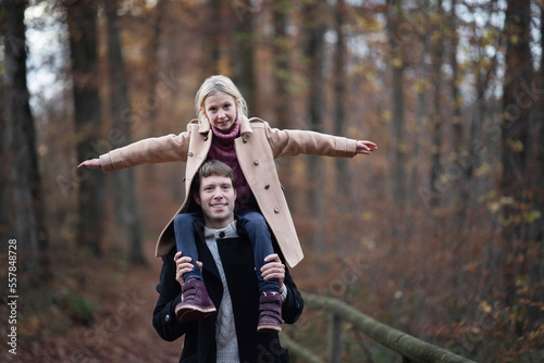 Happy father carrying daughter on shoulders in autumn forest photo