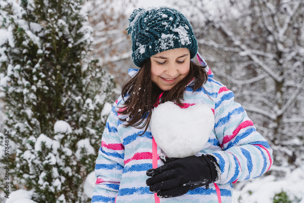Smiling girl holding heart-shaped snowball in winter Smiling girl holding heart-shaped snowball in winter