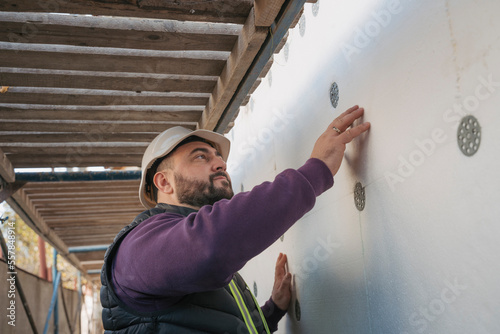 Construction worker examining polystyrene foam wall on site photo