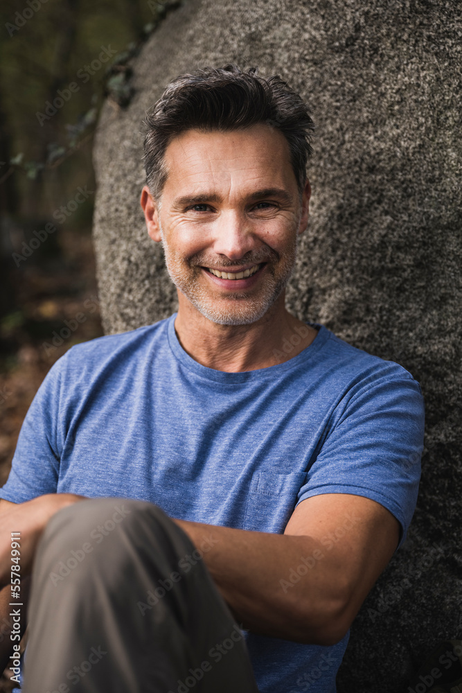 Happy mature man sitting in front of rock Happy mature man sitting in front of rock