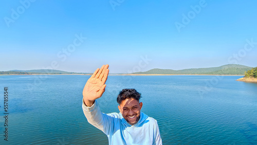Young man waving his hand at camera, Blue lake with blue sky scene Summer view