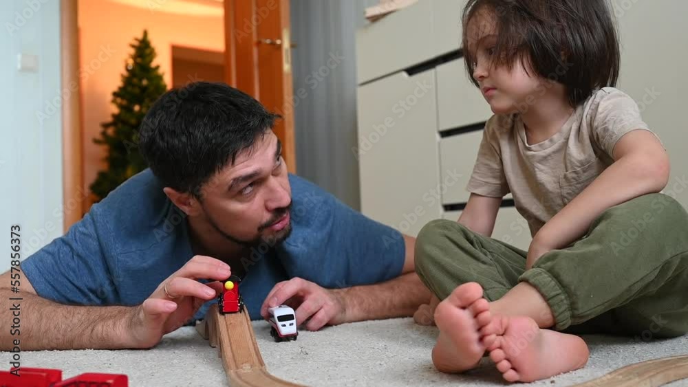 Father and son playing with toy train sitting on floor