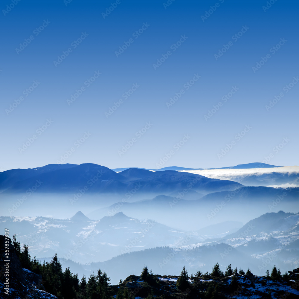 Foggy winter landscape in the mountains. Fantastic winter landscape. Aerial and morning view of snow covered mountain peaks rising over the foggy valleys. Dramatic overcast sky. Beauty world