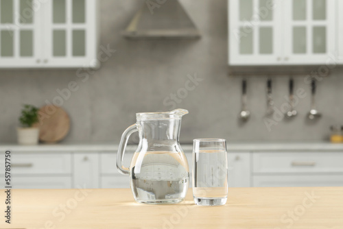 Glass and jug with water on wooden table in kitchen
