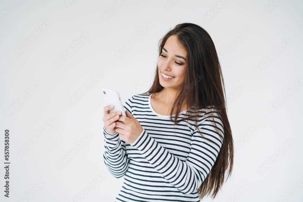 Young happy asian woman with long hair in striped longsleeve using mobile phone on white background isolated Young happy asian woman with long hair in striped longsleeve using mobile phone on white background isolated