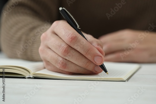 Man writing in notebook at white table, closeup