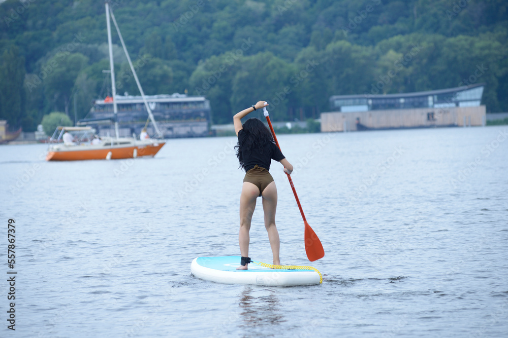 Naklejka premium Young woman in a swimsuit rowing a SUP board on the river