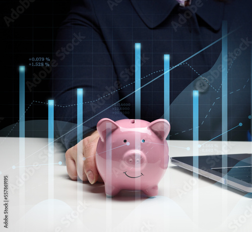 Woman in a suit sits at a table and works on a laptop, next to it is a ceramic piggy bank