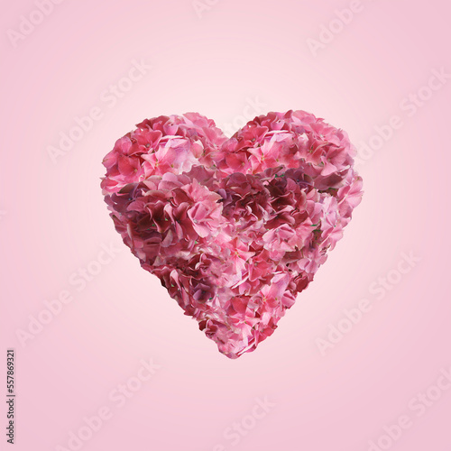 Heart made with pink flowers and petals at pink background