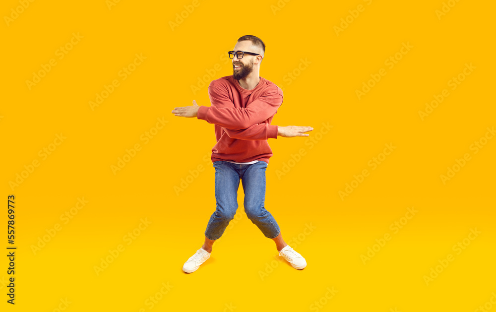 Cheerful, funny and energetic man showing humorous joking dance moves on orange background. Full length of young man in stylish casual clothes with funny expression crouching and waving his arms. Cheerful, funny and energetic man showing humorous joking dance moves on orange background. Full length of young man in stylish casual clothes with funny expression crouching and waving his arms.