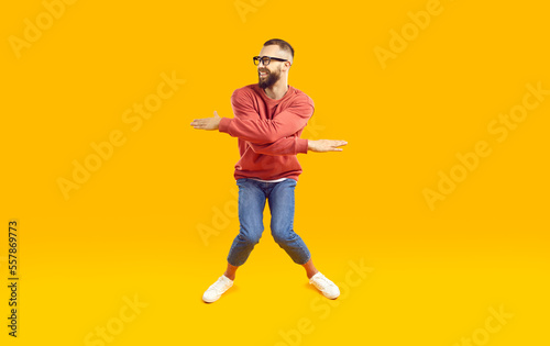 Cheerful  funny and energetic man showing humorous joking dance moves on orange background. Full length of young man in stylish casual clothes with funny expression crouching and waving his arms.