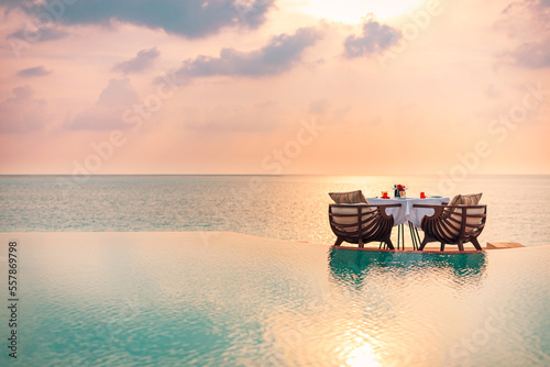 Seascape view under sunset light with dining table with infinity pool around. Romantic tranquil getaway for two, couple concept. Chairs, food and romance. Luxury destination dining, honeymoon template photo