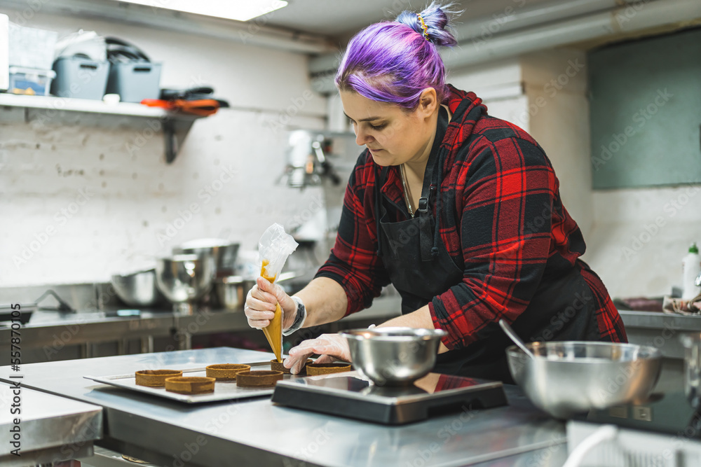 Female pastry chef wearing a apron decorating cake with a pastry bag with cream. Small baking business. High quality photo Female pastry chef wearing a apron decorating cake with a pastry bag with cream. Small baking business. High quality photo