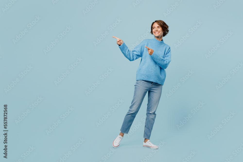 Full body young young woman wear knitted sweater point index finger aside indicate on workspace area copy space mock up isolated on plain pastel light blue cyan background. People lifestyle concept.